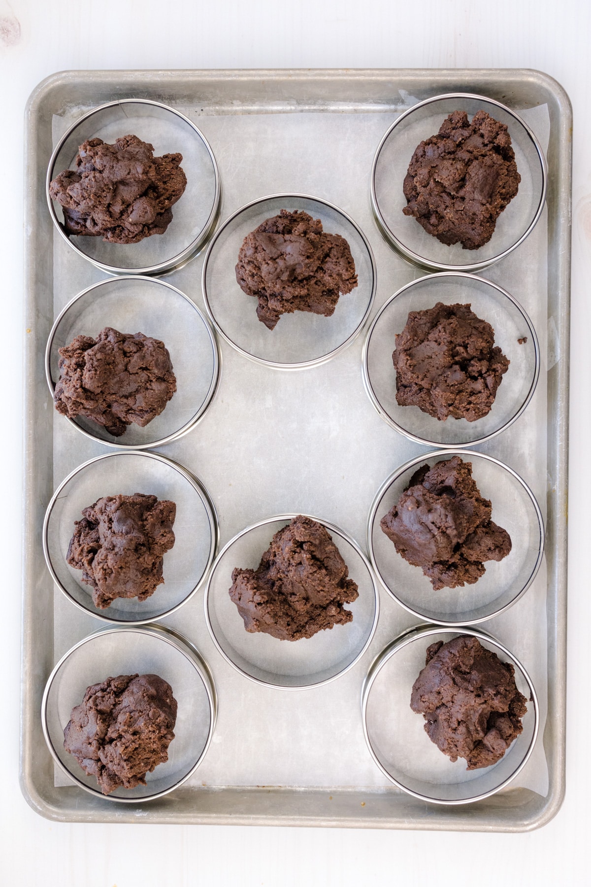 Overhead shot of cookie dough balls in cookie rings on a baking sheet.