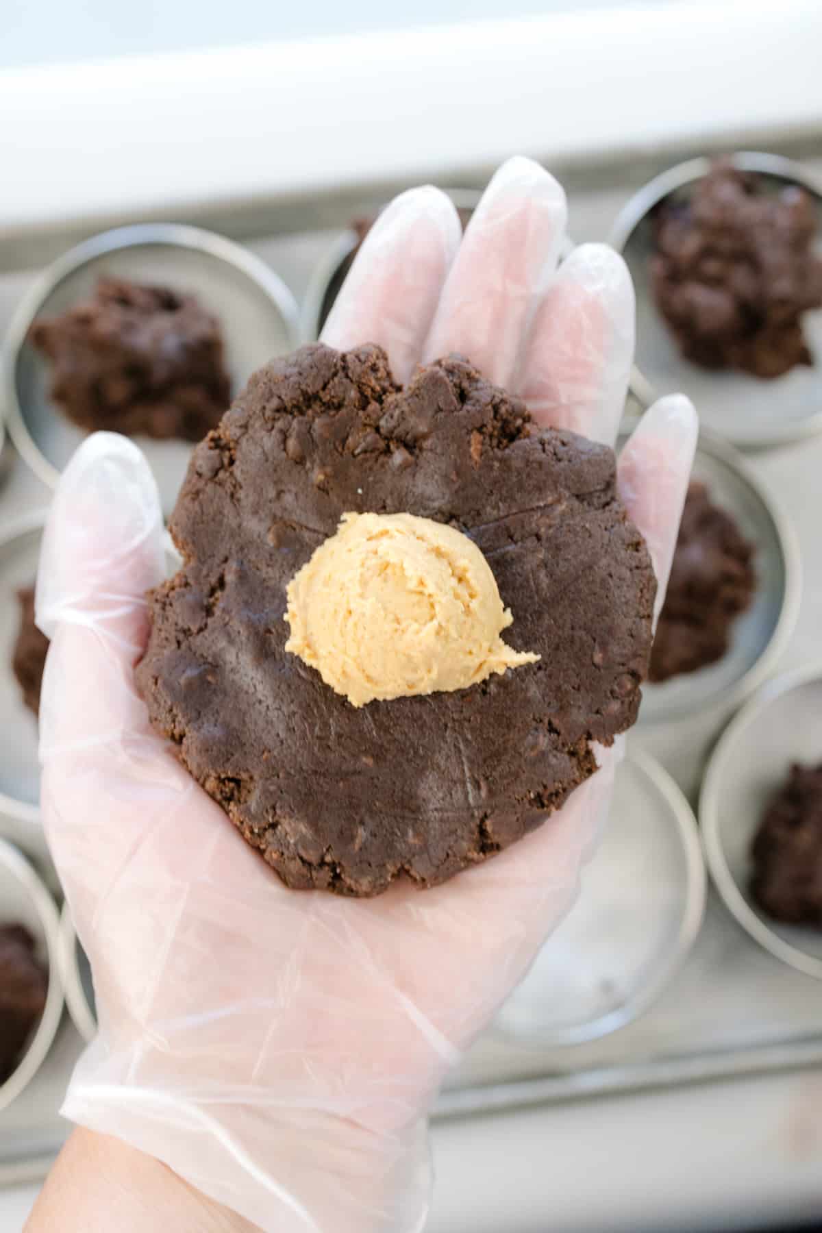 Close up shot of a hand holding chocolate cookie dough with a dollop of peanut butter mixture on it.