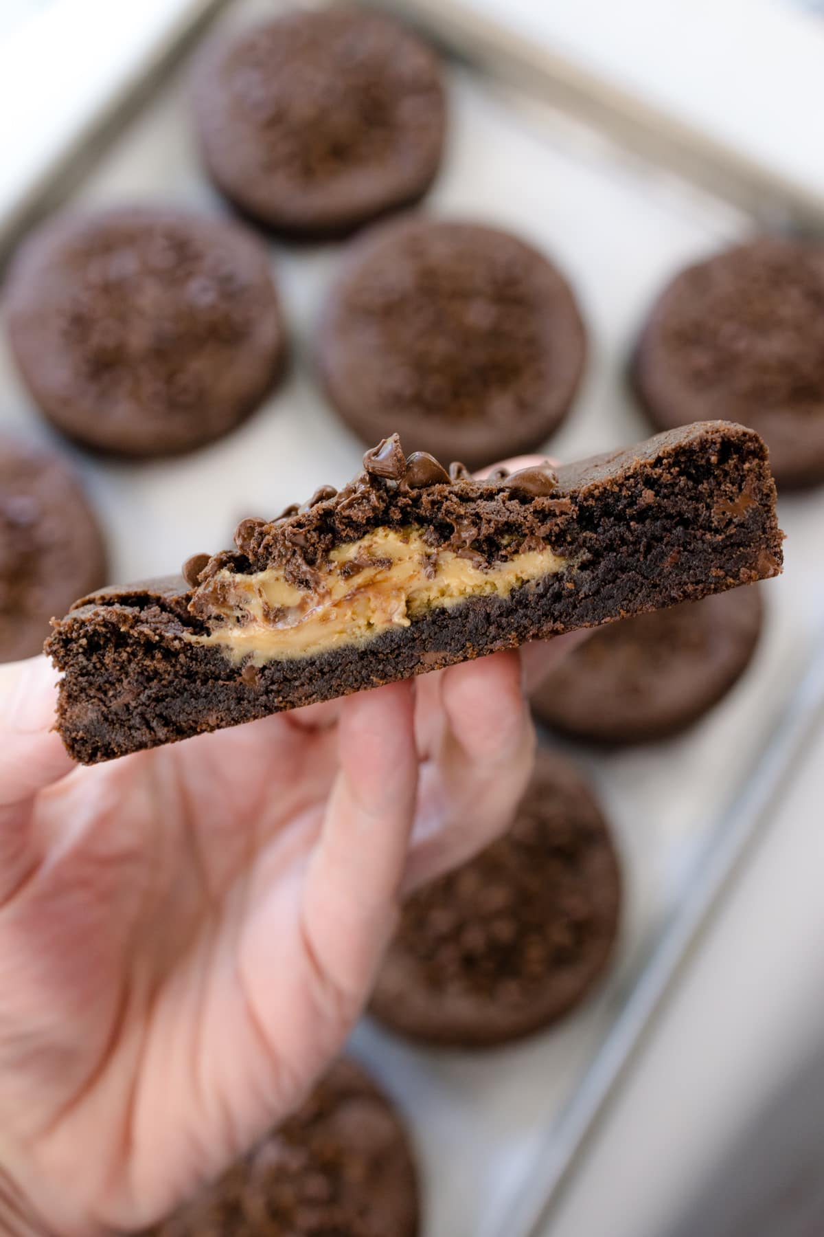 A close up shot of a hand holding a Peanut Butter Stuffed Chocolate Cookie that's cut open to reveal the middle.