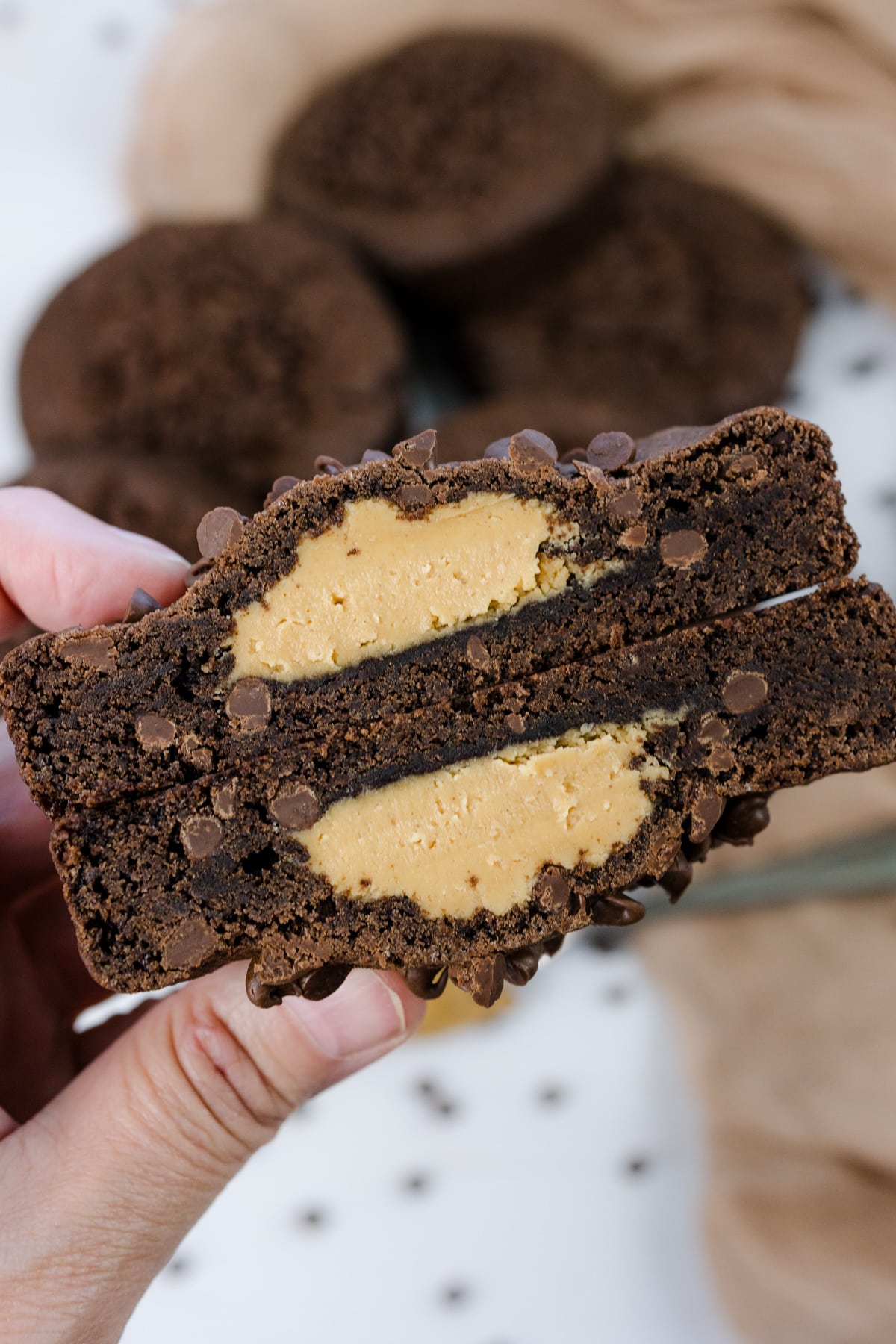 A close up shot of a hand holding a Peanut Butter Stuffed Chocolate Cookie that's cut open to reveal the middle.