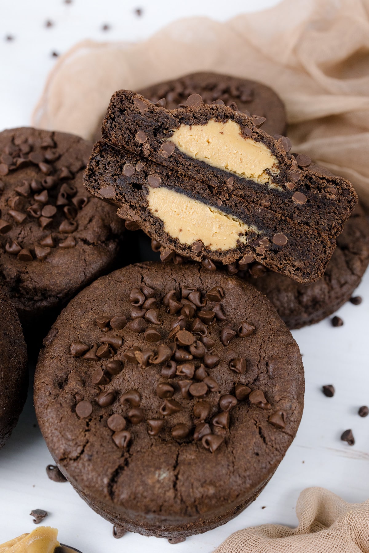 Close up shot of Peanut Butter Stuffed Chocolate Cookies on a white surface, and one is cut open to reveal the middle.