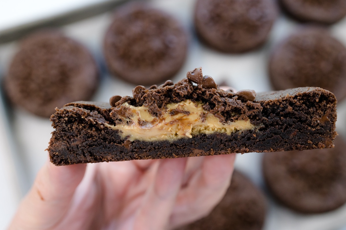 A close up shot of a hand holding a Peanut Butter Stuffed Chocolate Cookie that's cut open to reveal the middle.